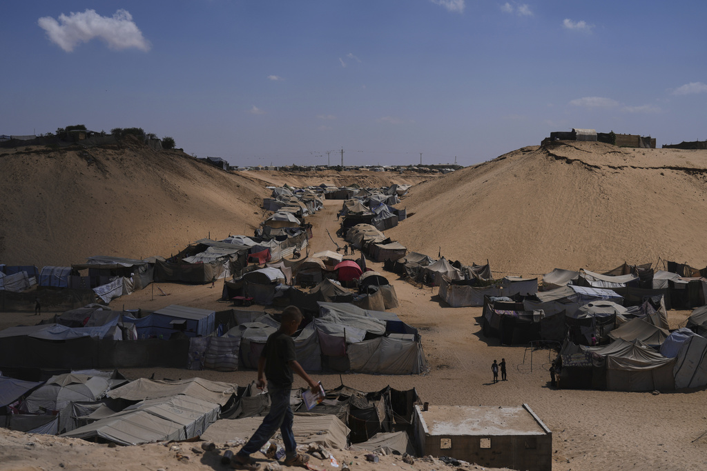 Displaced Palestinians walks through a tent camp in Muwasi, an area that Israel has designated as a safe zone, in Khan Younis southern Gaza Strip, Sunday, Sept. 21, 2025. (AP Photo/Jehad Alshrafi)