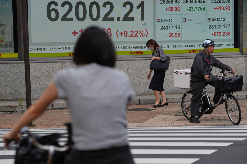 People wait to cross a street near an electronic board showing Japan's Nikkei index at a securities firm Friday, July 31, 2026. (AP Photo/Eugene Hoshiko)