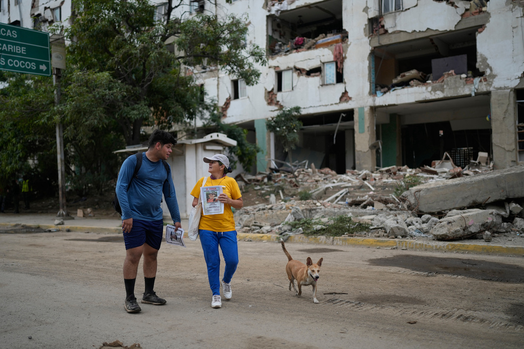 Pedro Gomez, left, walks through La Guaira, Venezuela, with a friend, asking people if they have seen his cousin, Andres Molina, who has been missing since the earthquakes, Saturday, Aug. 22, 2026. (AP Photo/Ariana Cubillos)