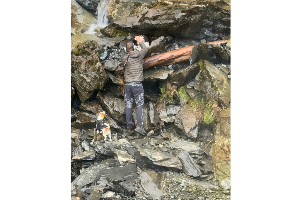 In this photo relased by Precision Helicopters Ltd, Wayne Holmes collects Molly from the edge of a waterfall as his dog Bingo, bottom left, stands beside on the Arahura River on the West Coast of the South Island of New Zealand, Tuesday, March 31, 2026. (Precision Helicopters Ltd via AP)