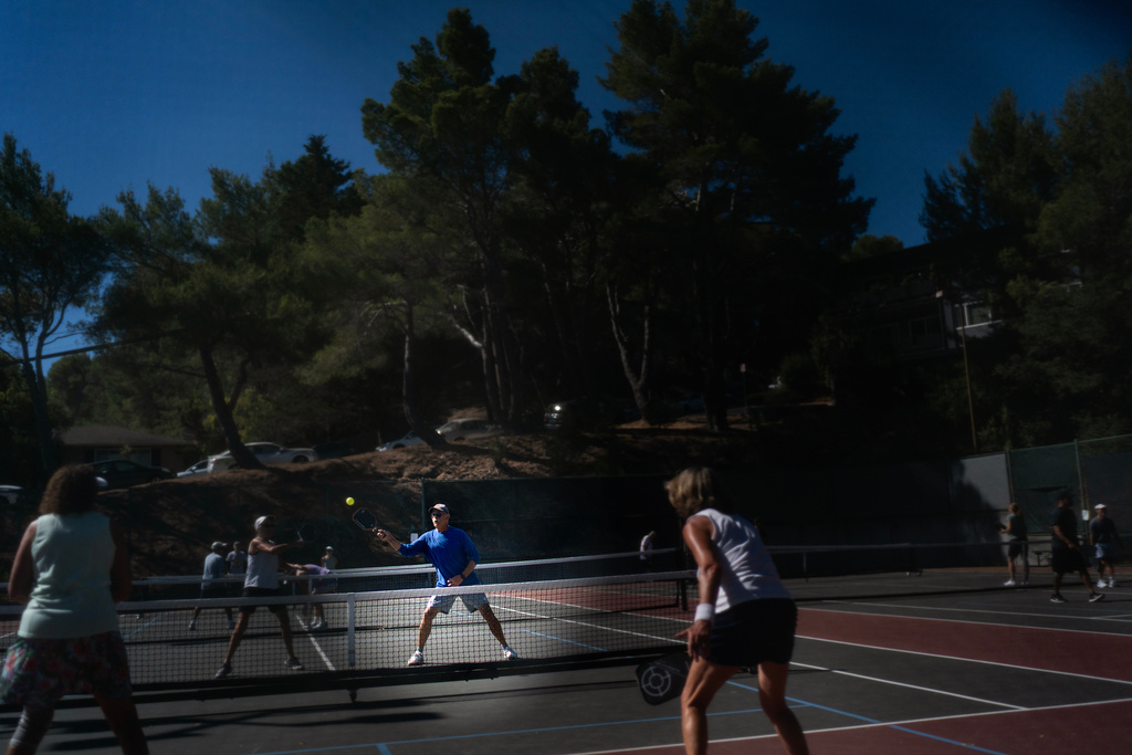 Christy Morrill, who lost decades of memories to autoimmune encephalitis, is seen through a hole in the fence playing pickleball, Tuesday, Aug. 19, 2025, in San Carlos, Calif. (AP Photo/David Goldman)