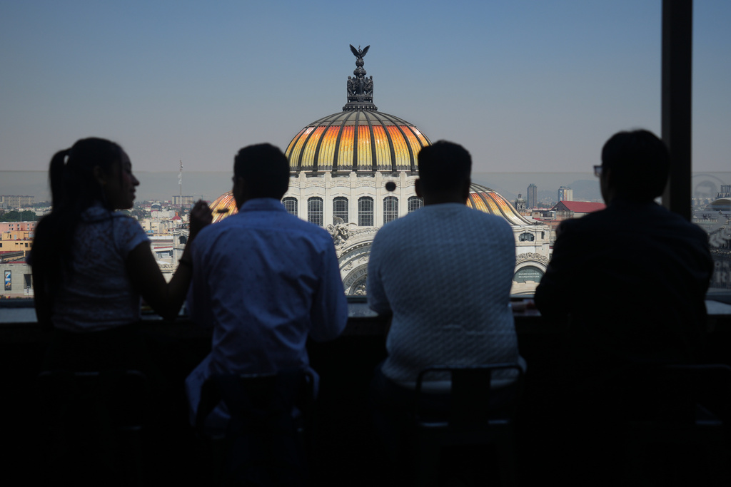 People sit at a rooftop bar overlooking Mexico City's Fine Arts Palace, where the Mexican coat of arms is visible atop the building's dome, Thursday, Nov. 13, 2025. (AP Photo/Claudia Rosel)