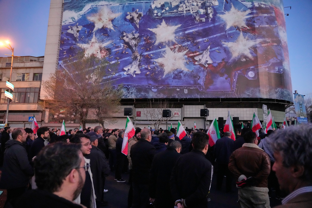 Government supporters gather in mourning after state TV officially announced the death of Iranian Supreme Leader Ayatollah Ali Khamenei, under a billboard with graphic showing a U.S aircraft carrier with damaged fighter jets on its deck, in Tehran, Iran, Sunday, March 1, 2026. (AP Photo/Vahid Salemi)
