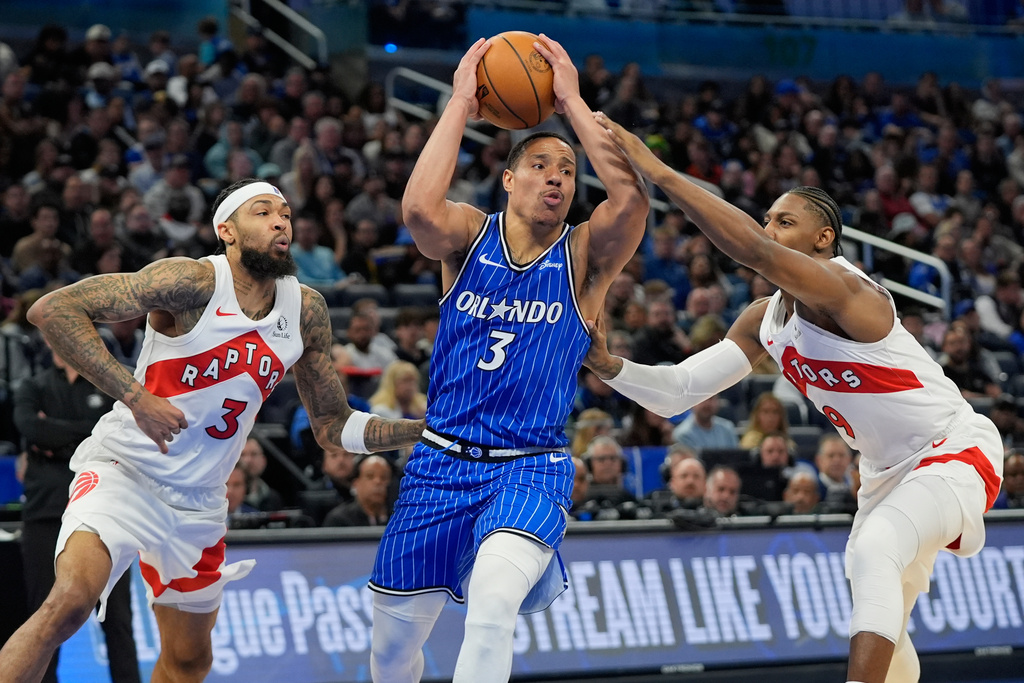 Orlando Magic guard Desmond Bane, center, drives against Toronto Raptors forward Brandon Ingram, left, and forward RJ Barrett during the first half of an NBA basketball game, Friday, Jan. 30, 2026, in Orlando, Fla. (AP Photo/John Raoux)