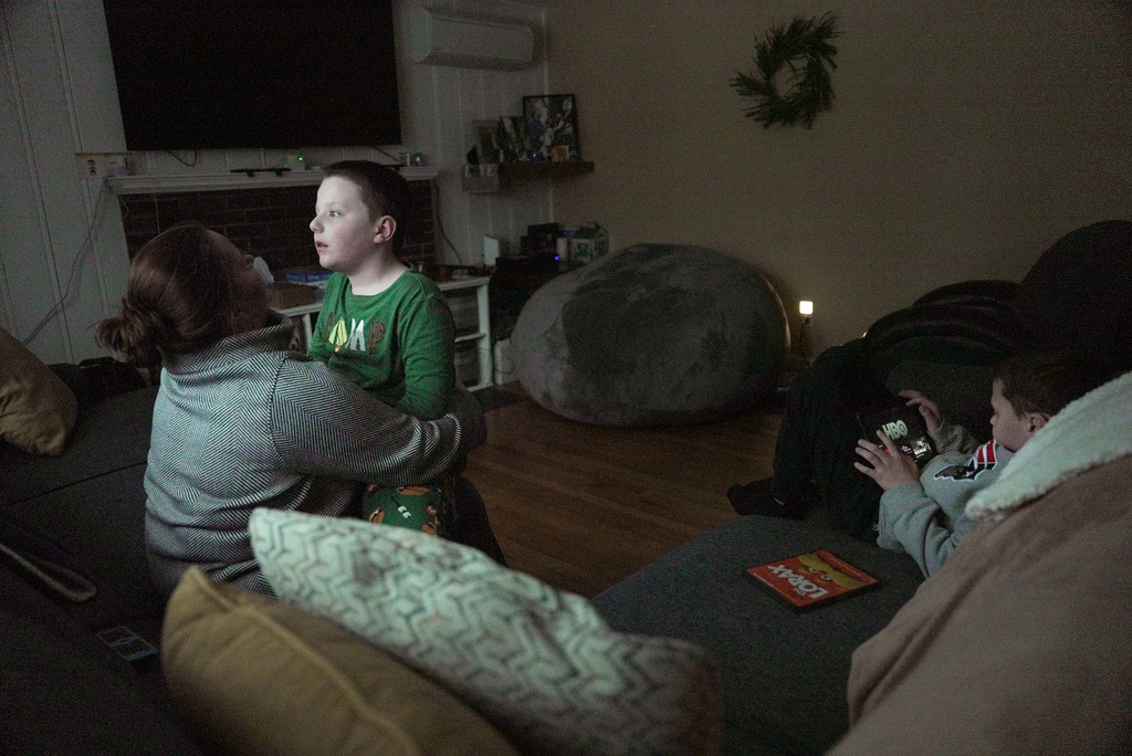 Ronan Murphy snuggles with his mom, Andrea, while looking at the snow falling outside his home while brother, Connor sits nearby in Ayer, Mass., on Saturday, Jan. 17, 2026. (AP Photo/Shelby Lum)