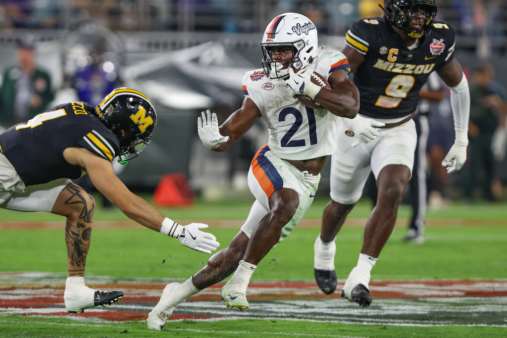 Virginia running back Harrison Waylee (21) shows a stiff-arm to Missouri safety Caleb Flagg, left, during the second quarter of the Gator Bowl NCAA college football game in Jacksonville, Fla., Saturday, Dec. 27, 2025. (AP Photo/Gary McCullough)