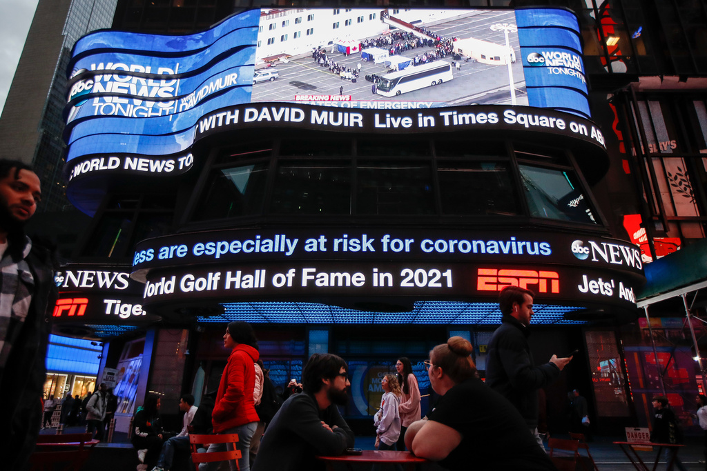 FILE - Pedestrians pass under a news ticker in Times Square on March 11, 2020, in New York. (AP Photo/John Minchillo, File)