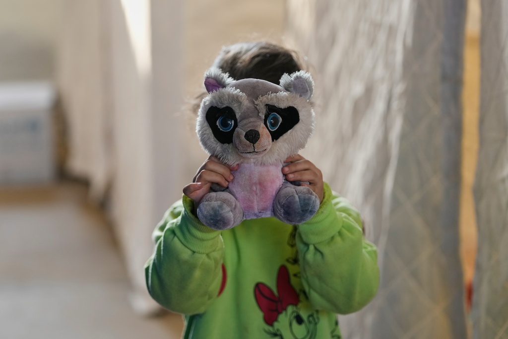 A displaced girl holds a stuffed toy to cover her face from a photographer while standing inside the Camille Chamoun Sports City Stadium, which has been turned into a shelter for people displaced by Israeli airstrikes in southern Lebanon and Dahiyeh, Beirut's southern suburbs, in Beirut, Lebanon, Tuesday, March 10, 2026. (AP Photo/Hassan Ammar)