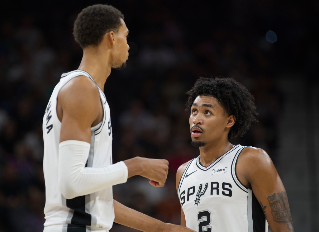 San Antonio Spurs center Victor Wembanyama, left, speaks with teammate Dylan Harper, right, during the first half of a preseason NBA basketball game against the Utah Jazz, Friday, Oct. 10, 2025, in San Antonio. (AP Photo/Darren Abate)