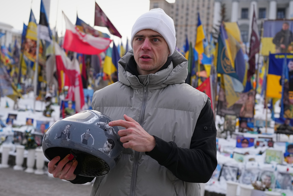 Ukrainian skeleton athlete Vladyslav Heraskevych holds his crash helmet as he stands outside an improvised memorial to fallen soldiers killed in Russia - Ukraine war at Independence square in Kyiv, Ukraine, Wednesday, Feb. 18, 2026. (AP Photo/Sergei Grits)
