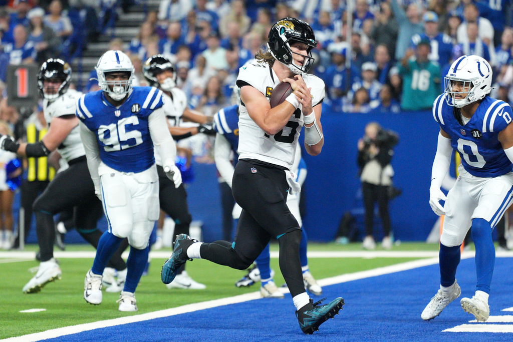 Jacksonville Jaguars quarterback Trevor Lawrence scores past Indianapolis Colts defensive tackle Adetomiwa Adebawore (95) and safety Camryn Bynum (0) during the second half of an NFL football game Sunday, Dec. 28, 2025, in Indianapolis. (AP Photo/AJ Mast)