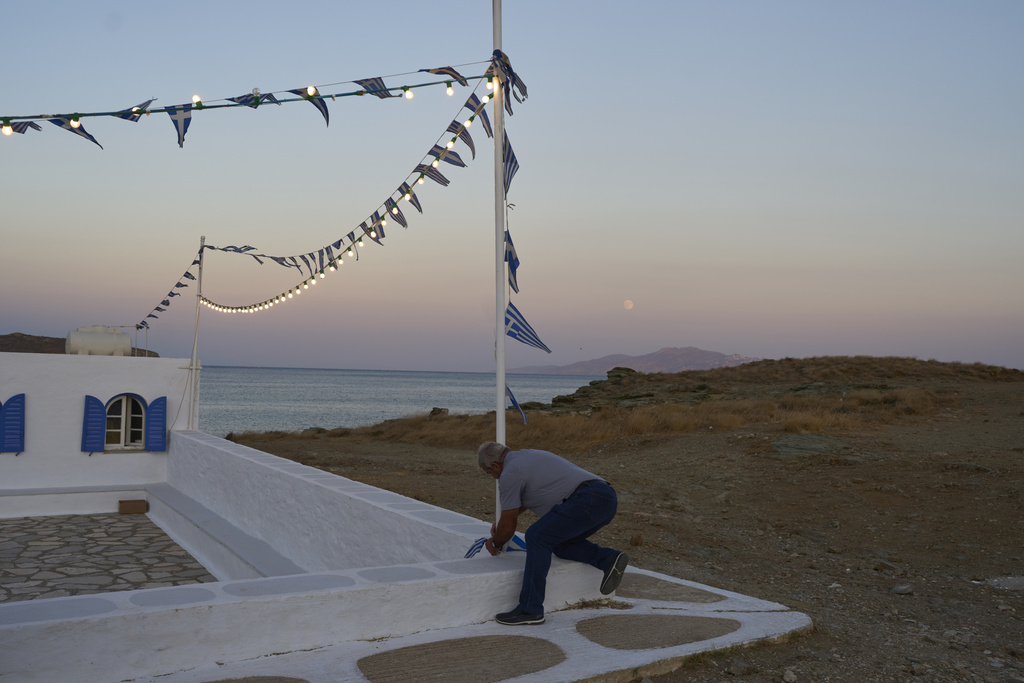 Zerar Delatolas fastens Greek flags to a pole outside the family-owned Agios Sostis chapel during its annual panigiri, on the island of Tinos, Greece, Saturday, Sept. 6, 2025. (AP Photo/Petros Giannakouris)