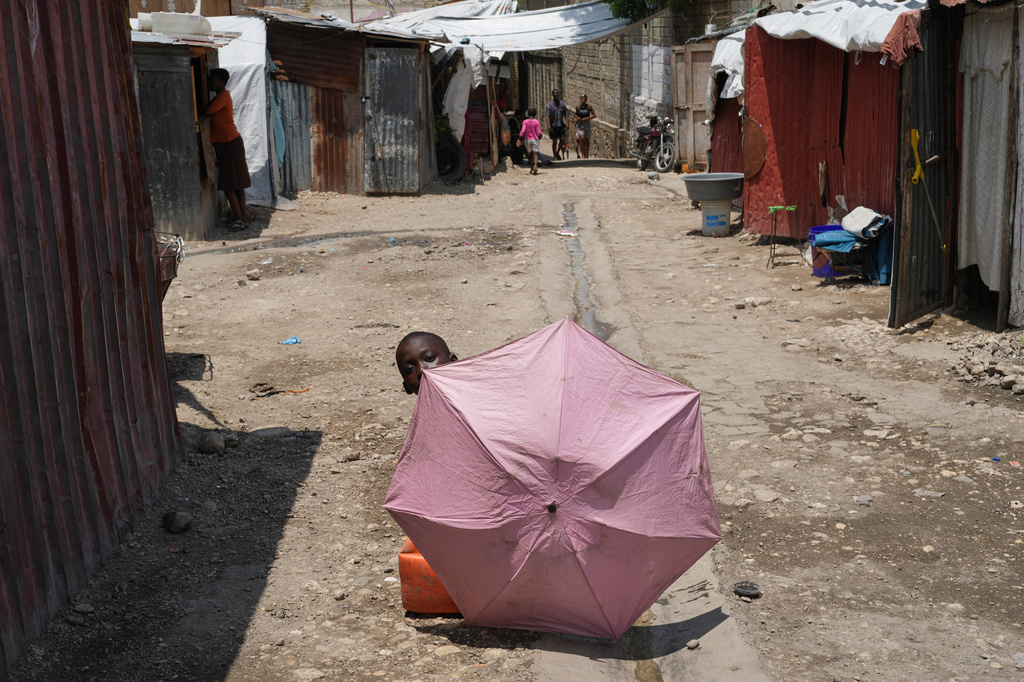 A youth using an umbrella to shade himself plays at a shelter for families displaced by gang violence in Port-au-Prince, Haiti, Monday, April 13, 2026. (AP Photo/Odelyn Joseph)