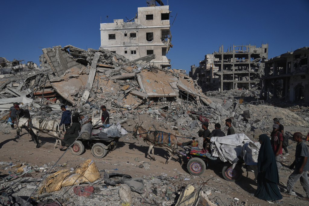 Displaced Palestinians ride donkey carts loaded with belongings past destroyed buildings in Gaza City, Saturday, Oct. 11, 2025, after Israel and Hamas agreed to a pause in their war and the release of the remaining hostages. (AP Photo/Abdel Kareem Hana)