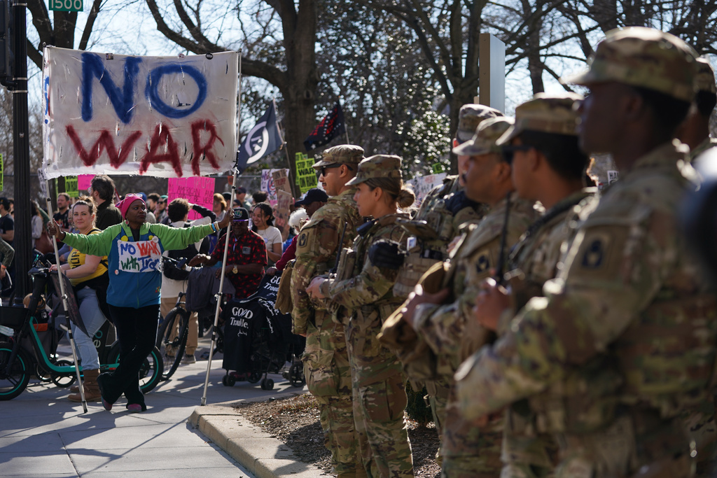 National Guard members watch as people protest near the White House against U.S. and Israeli strikes on Iran, Saturday, Feb. 28, 2026 in Washington. (AP Photo/Allison Robbert)
