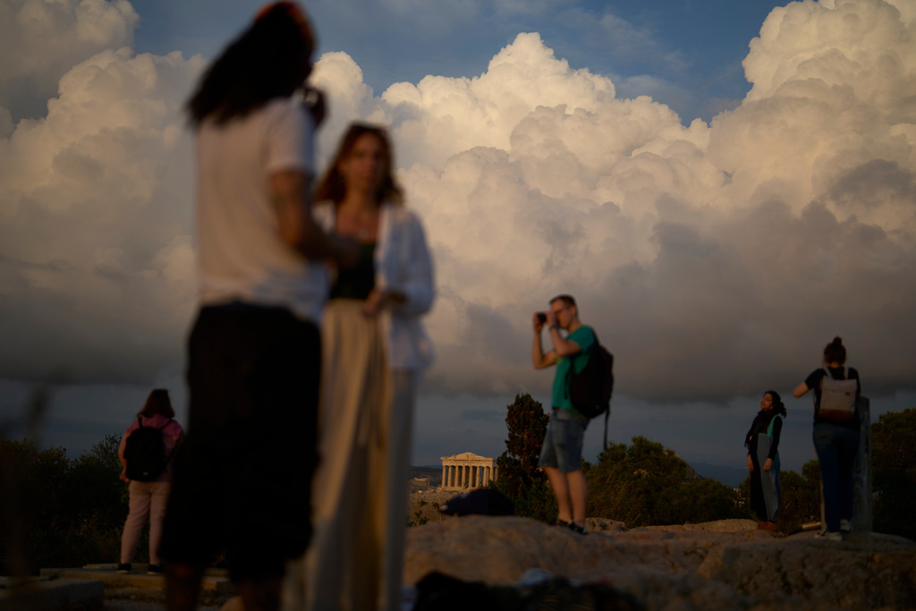 Tourists stand on Filopappos Hill with the ancient Parthenon atop the Acropolis in the background, in Athens, Tuesday, Oct. 21, 2025. (AP Photo/Petros Giannakouris)
