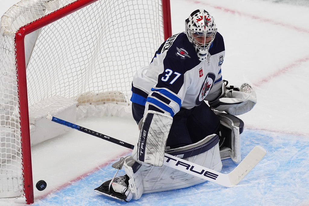 Winnipeg Jets goaltender Connor Hellebuyck allows a shot by Colorado Avalanche defenseman Brent Burns to go into the net for a goal in the first period of an NHL hockey game Friday, Dec. 19, 2025, in Denver. (AP Photo/David Zalubowski)