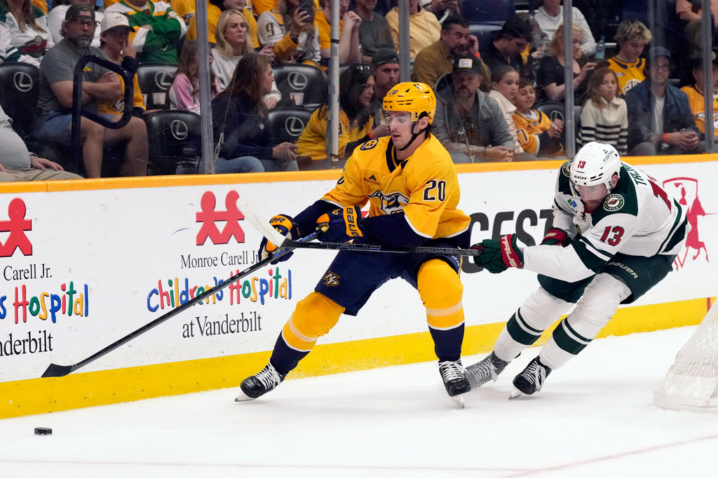 Nashville Predators defenseman Justin Barron (20) and Minnesota Wild center Yakov Trenin (13) chase the puck during the second period of an NHL hockey game Saturday, April 11, 2026, in Nashville, Tenn. (AP Photo/Mark Humphrey)