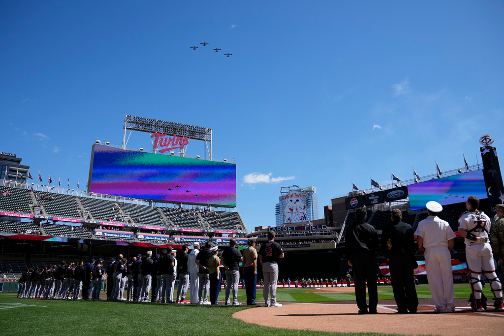Fans and members of the military stand for the playing of the national anthem as planes perform a flyover prior to a baseball game between the Minnesota Twins and the Cleveland Guardians, Sunday, Sept. 13, 2026, in Minneapolis. (AP Photo/Joseph Scheller)