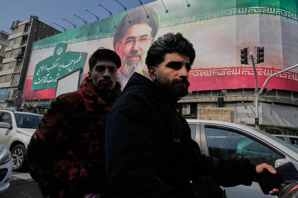 Two men ride their motorbike past a billboard of the Iranian Supreme Leader Ayatollah Mojtaba Khamenei in downtown Tehran, Iran, Saturday, March 14, 2026. (AP Photo/Vahid Salemi)