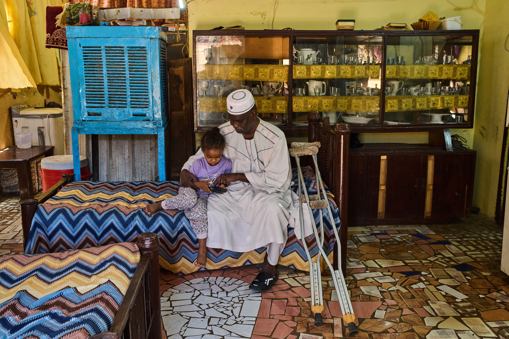 Tariq Abuzeid, 52, who lost his leg in a shelling attack, sits with his granddaughter in the family living room in Omdurman, on the outskirts of Khartoum, Sudan, Saturday, April 25, 2026. (AP Photo/Bernat Armangue)