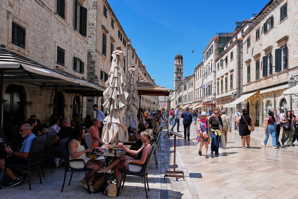 People sit in a cafe as others walk on the main street of Stradun in old town Dubrovnik, Croatia, Monday, April 27, 2026. (AP Photo/Darko Bandic)