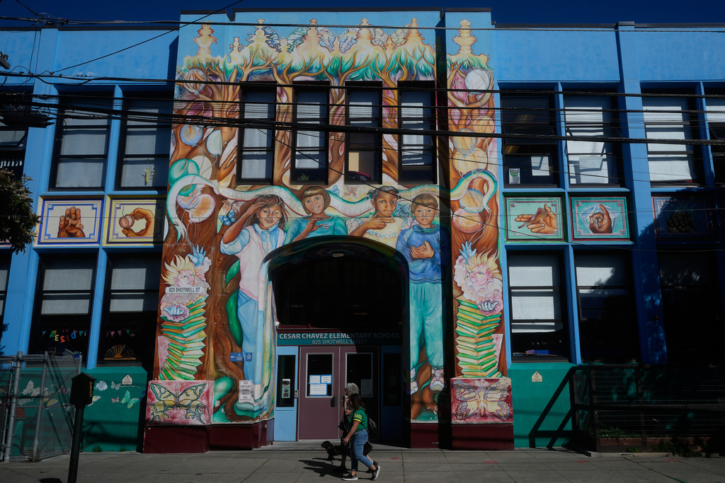 Pedestrians walk below a mural outside of César Chavez Elementary School in San Francisco, Wednesday, March 18, 2026. (AP Photo/Jeff Chiu)