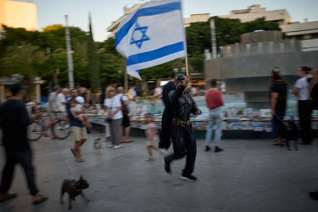 A man dressed as Batman waves an Israeli flag as people watch photos of Israelis who were killed in the Oct. 7, 2023 deadly Hamas attack on Israel, at a memorial marking two years anniversary of the assault, in Tel Aviv, Israel, Tuesday, Oct. 7, 2025. (AP Photo/Emilio Morenatti)