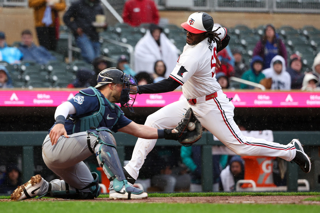 Minnesota Twins designated hitter Josh Bell, right, slides safely into home plate as Seattle Mariners catcher Mitch Garver, left, fields the ball during the second inning of a baseball game, Monday, April 27, 2026, in Minneapolis. (AP Photo/Matt Krohn)