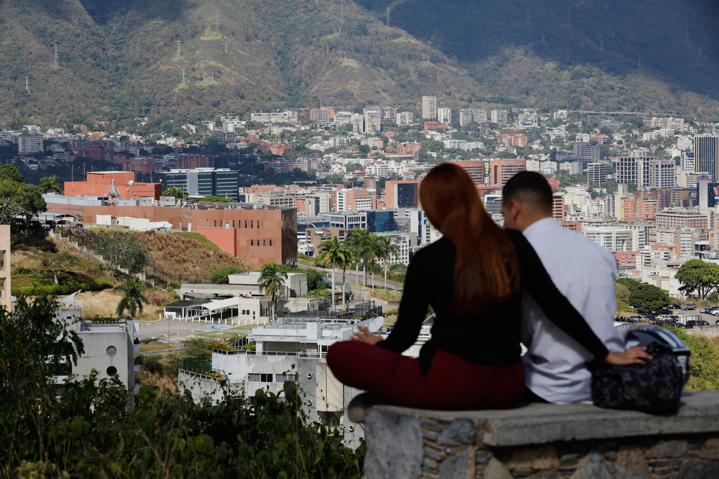 A couple sits on a bench at a viewpoint overlooking the U.S. embassy, center left, in Caracas, Venezuela, Friday, Jan. 9, 2026. (AP Photo/Cristian Hernandez)