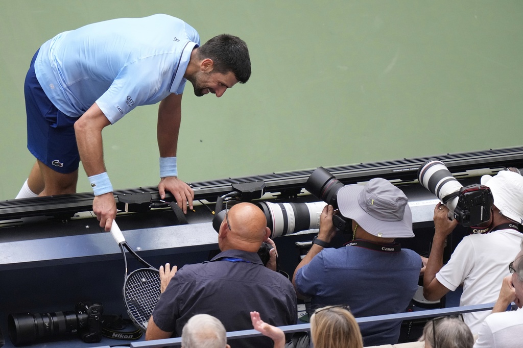 Novak Djokovic, of Serbia, runs into the photgraphers box against Carlos Alcaraz, of Spain, during the men's singles semifinals of the U.S. Open tennis championships, Friday, Sept. 5, 2025, in New York. (AP Photo/Frank Franklin)