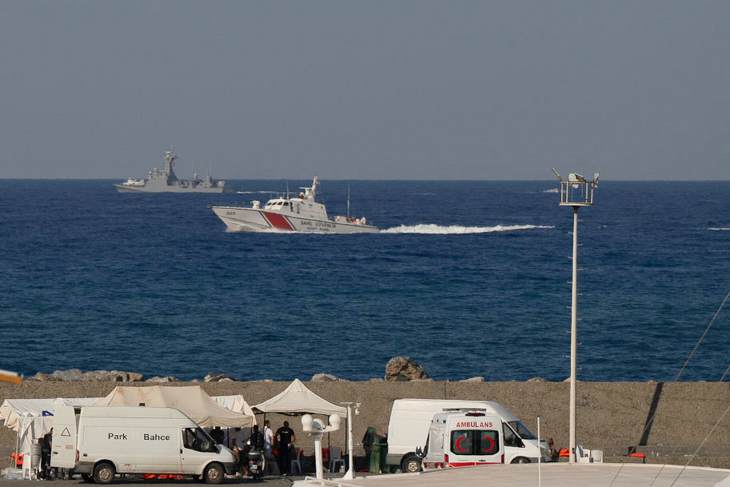 Vessels sail near the port of Kyrenia as an ambulance is parked on the waterfront in the Turkish-occupied northern part of Cyprus, Sunday, Aug. 30, 2026, after a catamaran-style ferry overturned off the island's northern coast. (AP Photo/Nedim Enginsoy)