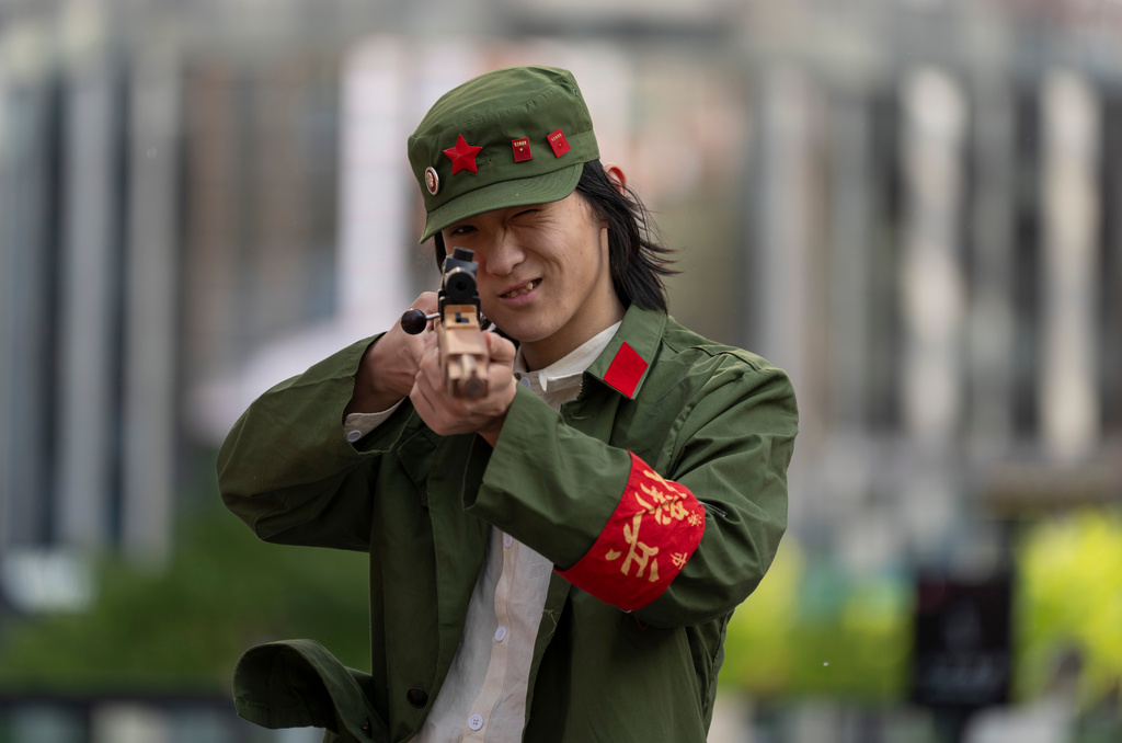 A volunteer wearing Communist-themed clothing and memorabilia poses with a wooden rifle at an outdoor market in Beijing, Friday, May 8, 2026. (AP Photo/Ng Han Guan)