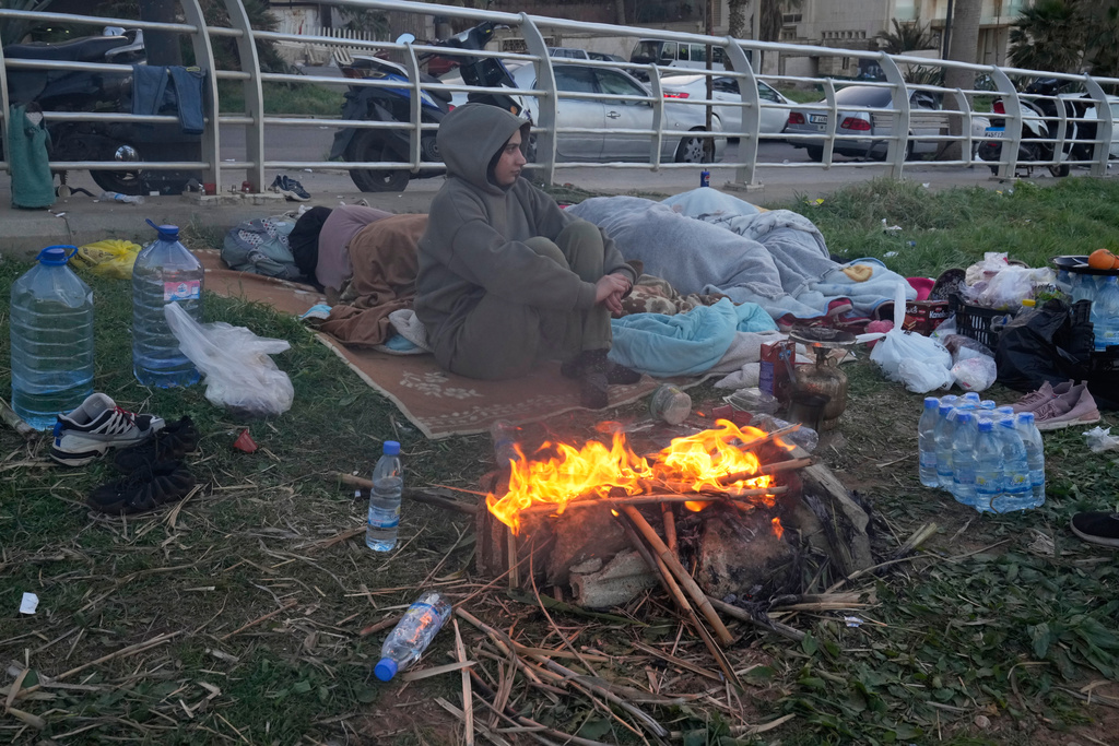 A displaced woman fleeing Israeli airstrikes in Beirut's southern suburb of Dahiyeh warms herself near fire on the Beirut corniche, Lebanon, Friday, March 6, 2026. (AP Photo/Hussein Malla)