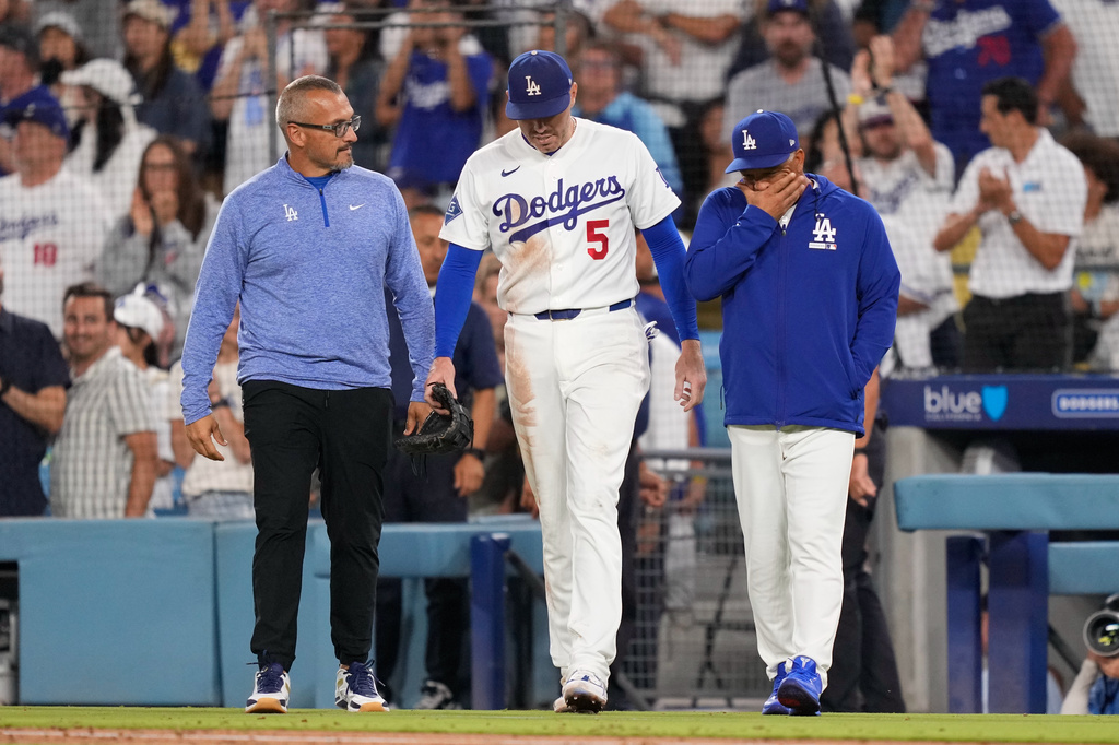 Los Angeles Dodgers first baseman Freddie Freeman, center, walks back on to the field accompanied by manager Dave Roberts, right, and trainer Greg Barajas after he fell into the dugout while trying to catch a foul ball hit by Kansas City Royals' Isaac Collins during the eighth inning of a baseball game Wednesday, Aug. 12, 2026, in Los Angeles. (AP Photo/Mark J. Terrill)