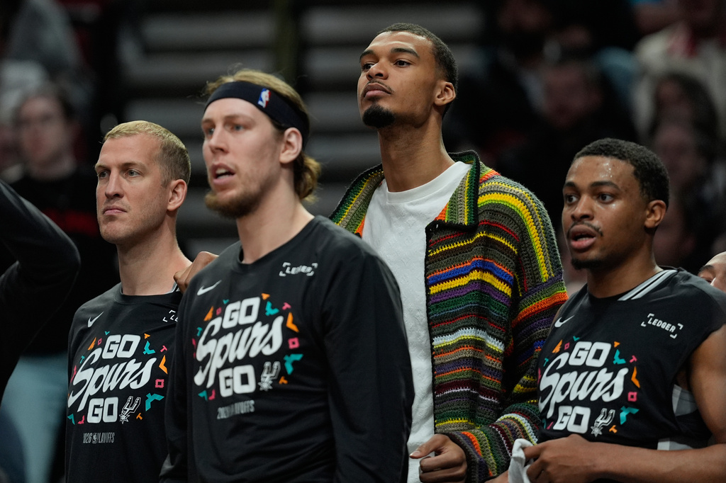 San Antonio Spurs forward Victor Wembanyama, center, wears street cloths on the bench as he sits out Game 3 of a first-round NBA playoffs basketball series against the Portland Trail Blazers in Portland, Ore, Friday, April 24, 2026. (AP Photo/Jenny Kane)