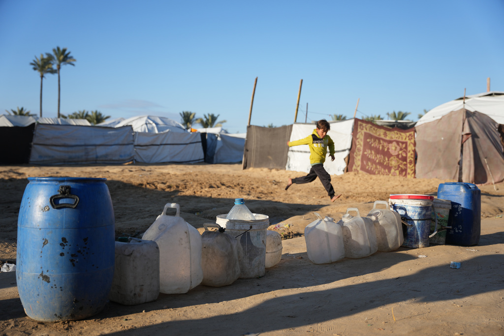 A displaced Palestinian boy runs past empty water barrels as residents wait for a drinking water delivery in Deir al-Balah, Gaza Strip, Saturday, Jan. 17, 2026. (AP Photo/Abdel Kareem Hana)