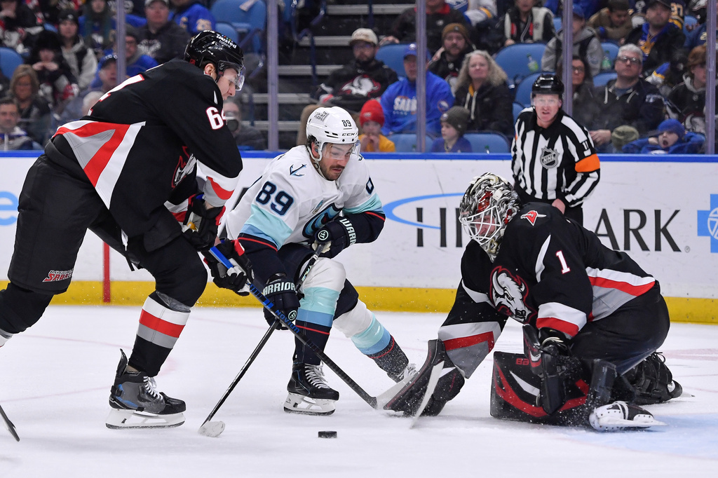 Seattle Kraken center Frederick Gaudreau, center, skates the puck toward the goal between Buffalo Sabres goalie Ukko-Pekka Luukkonen, right, and defenseman Logan Stanley, left, during the second period of an NHL hockey game Saturday, March 28, 2026, in Buffalo, N.Y. (AP Photo/Adrian Kraus)