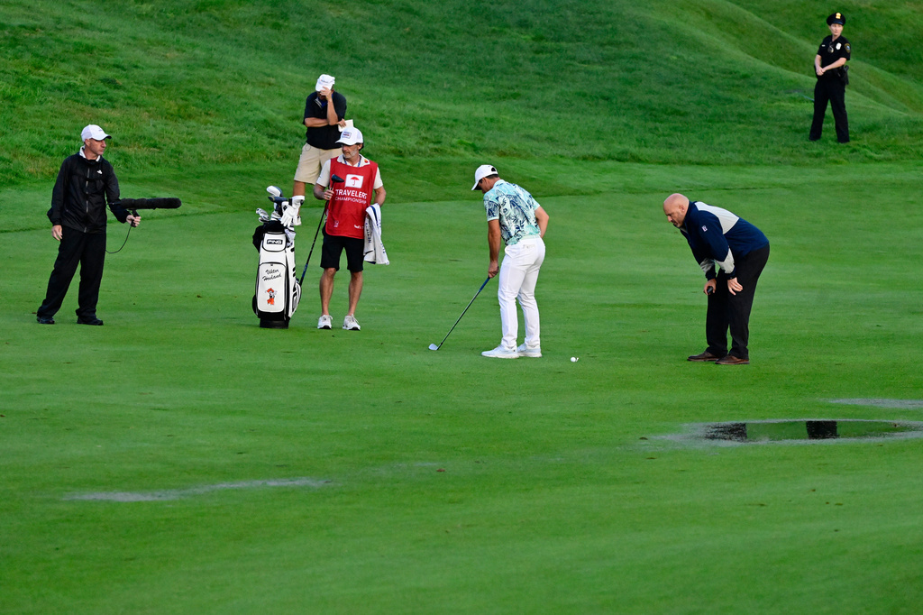 Viktor Hovland, center, of Norway, moves his ball due to standing water without penalty on the 18th fairway during the final round of the Travelers Championship golf tournament at TPC River Highlands, Sunday, June 28, 2026, in Cromwell, Conn. (AP Photo/Jessica Hill)