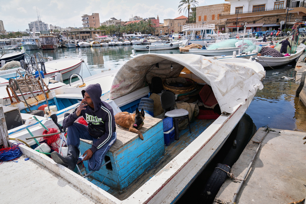 A fisherman who did not flee his city despite Israeli airstrikes, sits with his dog on his boat in the southern port city of Tyre, Lebanon, Thursday, March 26, 2026. (AP Photo/Hussein Malla)