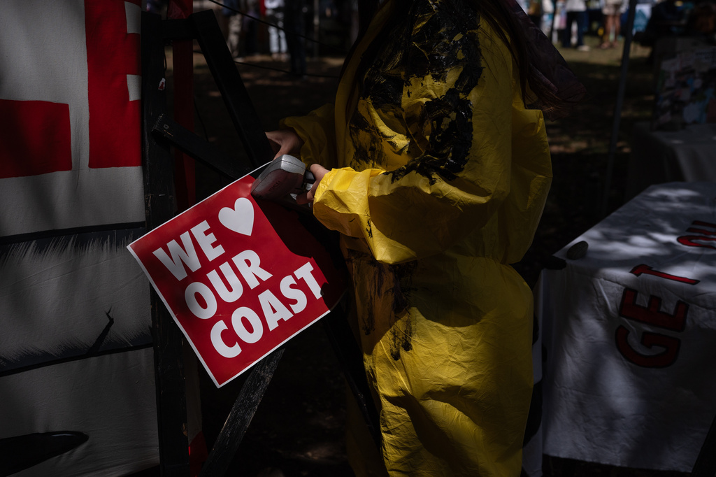 Activist Isabella Pena uses a stapler to post a sign opposing offshore oil operations by Sable Offshore Corp. during the Santa Barbara Earth Day Festival in Santa Barbara, Calif., Sunday, April 26, 2026. (AP Photo/Jae C. Hong)