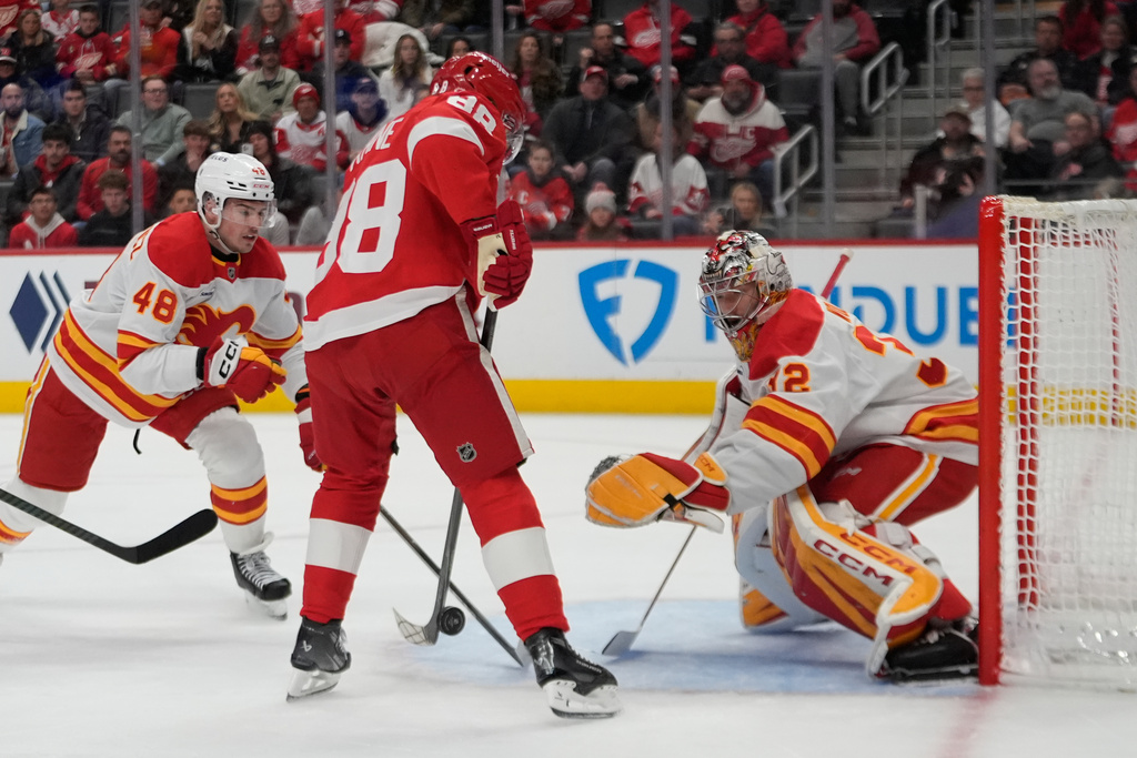 Calgary Flames goaltender Dustin Wolf (32) stops a Detroit Red Wings right wing Patrick Kane (88) shot as Hunter Brzustewicz (48) looks on in the first period of an NHL hockey game Monday, March 16, 2026, in Detroit. (AP Photo/Paul Sancya)
