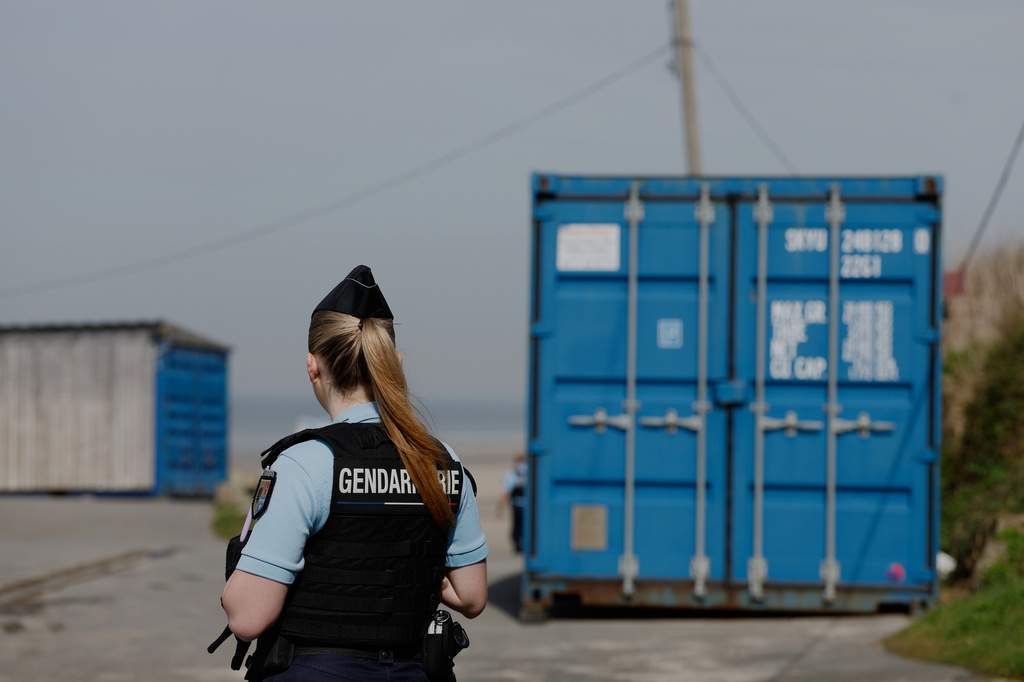 A police officer stands guard after a migrant taxi-boat accident, in Equihen-Plage, northern France. Thursday, April 9, 2026. (AP Photo/Jean-Francois Badias)