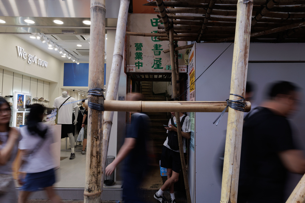 Pedestrians pass a narrow street entrance leading to Greenfield Bookstore beneath bamboo scaffolding in Hong Kong Friday, Aug. 14, 2026. (AP Photo/May James)