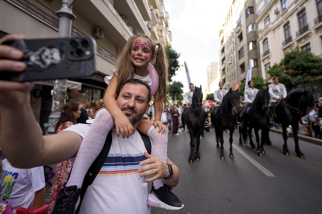 A man takes a selfie photograph with a child during a parade marking the day when the Romanian capital was first mentioned in historical records, 566 years ago, in Bucharest, Romania, Saturday, Sept. 20, 2025. (AP Photo/Andreea Alexandru)