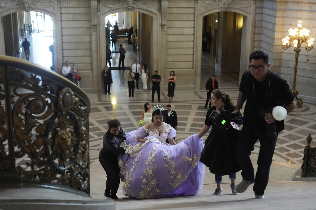 Leyla Portillo gets help with her gown from her mother Olga Portillo, left, and videographer-photographer Paola Soto, second from right, as Soto's husband and photographer Cesar Lopez, far right, walks ahead during her quinceañera portrait session at City Hall in San Francisco, Monday, April 28, 2025. (AP Photo/Jeff Chiu)