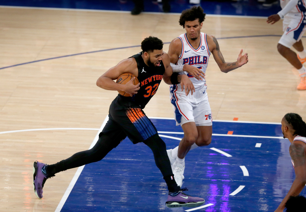 New York Knicks center Karl-Anthony Towns, left, dribbles past Philadelphia 76ers forward Dominick Barlow during the first half of an NBA basketball game, Friday, Dec. 19, 2025, in New York. (AP Photo/John Munson)