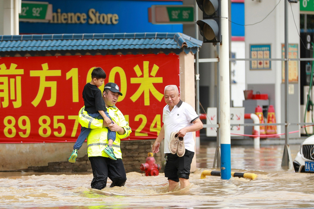 In this photo released by Xinhua News Agency, a police officer holds a boy as he wades through a flooded street in Duyun city, southwestern China's Guizhou Province on Tuesday, May 19, 2026. (Xiao Wei/Xinhua via AP)