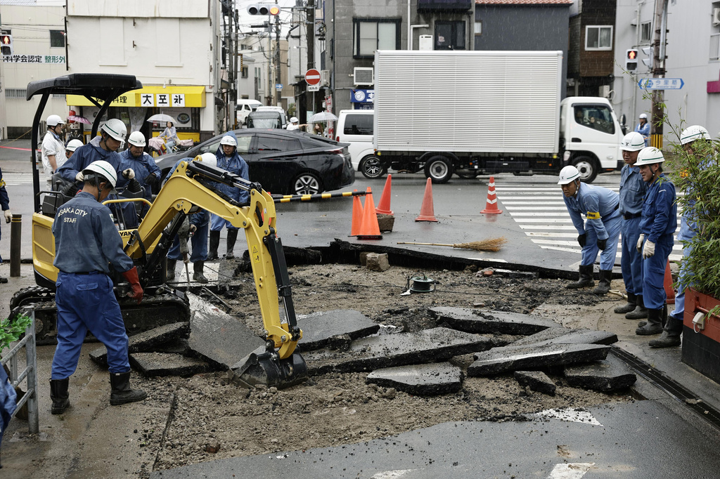 City workers repair a road damaged by water from a manhole following heavy rain, in Osaka, western Japan, Friday, June 26, 2026. (Kyodo News via AP)