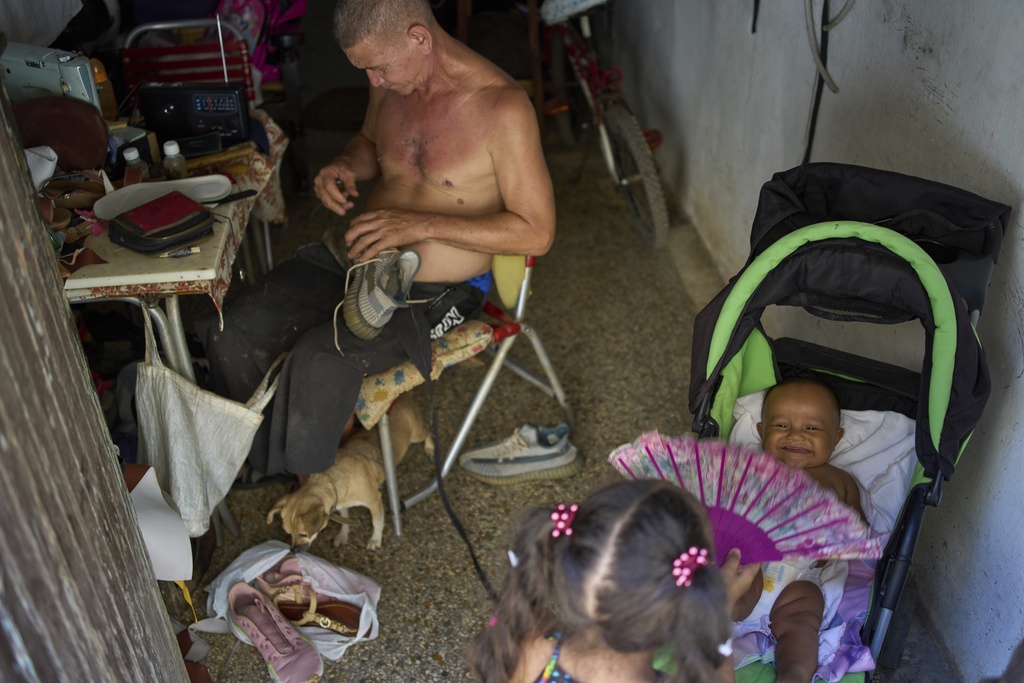 A girl cools a baby off with a fan as a man repairs shoes during a blackout in Havana, Wednesday, Sept. 10, 2025. (AP Photo/Ramon Espinosa)